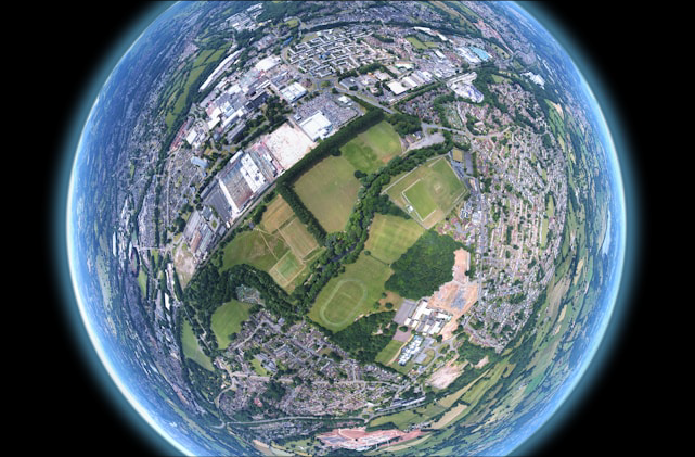 Kalasilm-efektiga satelliidifoto linnast ja rohealadest, nähtuna Maa kumeruse taustal.